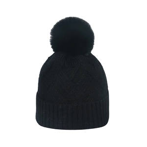Détail de la maille épaisse et du pompon en fausse fourrure sur ce bonnet noir d'hiver