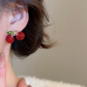 Close-up of cherry stud earrings featuring red resin fruit and green crystal leaves