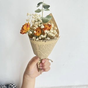 Hand holding a mini bouquet of orange dried roses and gypsophila in newspaper wrap