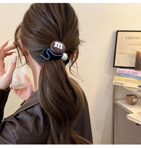 Détail d'un chouchou marron style chocolat avec lettre m et perle blanche sur cheveux