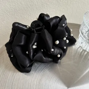 Dettaglio di una grande molletta per capelli a fiocco in raso nero con perle bianche