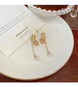 Detail view of long gold earrings featuring pink tulip flowers and delicate pearl pendants