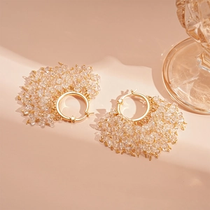 Detail of 18k gold plated star earrings with crystal tassels next to a glass cup