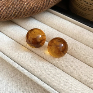 Detail of spherical amber resin earrings featuring unique marbled tortoiseshell texture