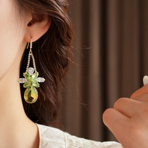Detail of model wearing emerald green water drop zircon earrings in golden floral design