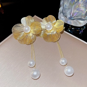 Detailed macro view of golden floral earrings with elegant long tassels and white pearls
