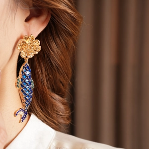 Detailed close-up of a vintage gold fish drop earring with blue and green enamel on a model
