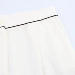 Detail of high-waist white shorts with black contrast piping and cotton linen texture