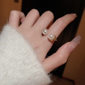 Detail of elegant gold-toned double pearl open ring worn with a soft white knitted sweater