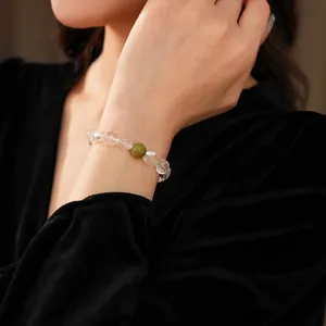 Bracelet de perles en cristal blanc avec pierre verte porté au poignet sur velours noir