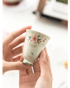 Detailed close-up of a hand-painted peach blossom ceramic teacup held by both hands