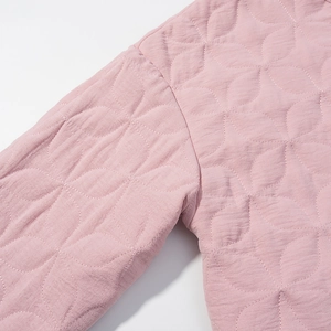 Macro detail of pink quilted jacket featuring floral stitch patterns and woven fabric texture