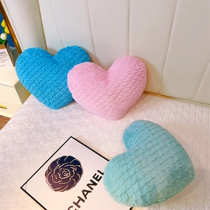Texture détaillée de coussins en peluche en forme de cœur rose, bleu et vert sur un lit