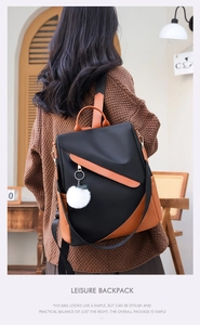 Chic black and brown patchwork backpack with white pompom charm on a model in a cafe