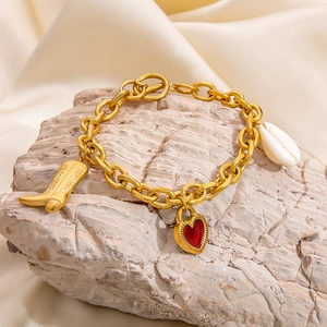 Gold chain bracelet with heart, shell and cowboy boot charms on a textured stone