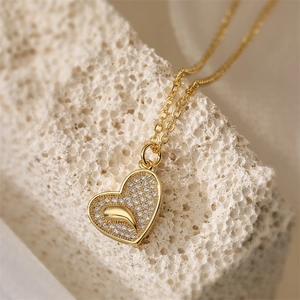Close-up of gold-plated heart pendant with zircons resting on a textured coral stone