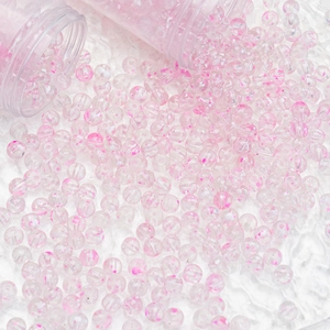 Macro detail of clear 10mm glass beads with pink floral patterns in plastic containers