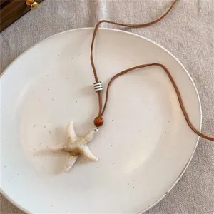 Détail du collier pendentif étoile de mer avec cordon marron et perles sur assiette céramique