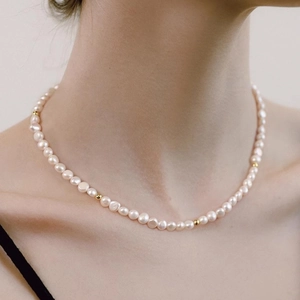 Detailed close-up of natural pearl necklace with gold beads on female neck
