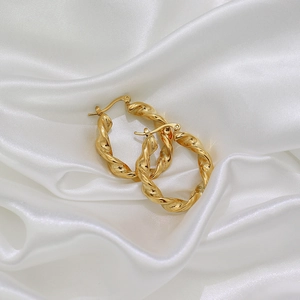 Détail de boucles d'oreilles créoles torsadées dorées sur un tissu en soie blanche