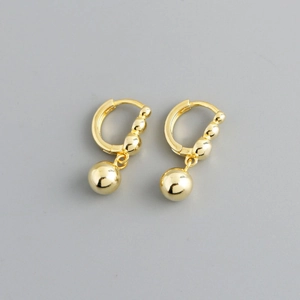 Detail view of gold hoop earrings featuring polished round bead charms in a studio setting