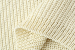 Macro shot of cream-colored chunky ribbed knit fabric with soft textured finish