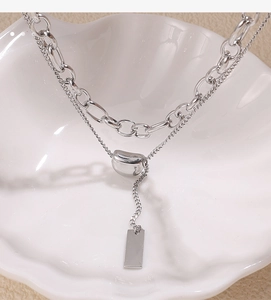 Macro shot of silver layered necklace with bean pendant and rectangular tag on shell tray