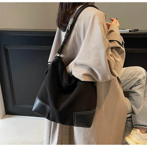 Detail of black suede tote bag with white contrast stitching and adjustable metal buckle