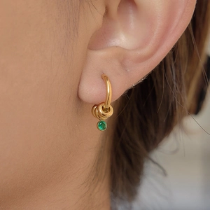 Gros plan d'une boucle d'oreille en acier inoxydable doré 18K avec zircon vert sur mannequin