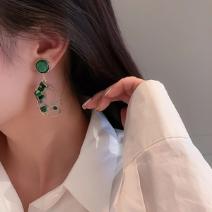 Close-up of irregular hollow earrings with green stones and gold metal plating