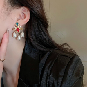Detail view of retro gold earrings with green and red gems and hanging triple pearls