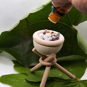 Close-up of essential oil being dropped onto a wooden diffuser with colored stones