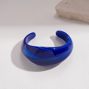 Close-up of a wide dark blue acrylic open bangle with marble texture and sand patterns