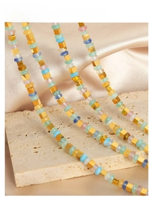 Détail de perles colorées et d'entretoises carrées dorées sur un collier en acier titane