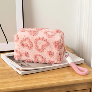 Detailed close-up of pink plush makeup bag featuring soft heart pattern and zipper strap