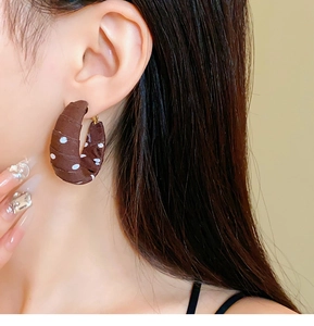 Detail of coffee brown fabric C-shaped earrings with white polka dots on model