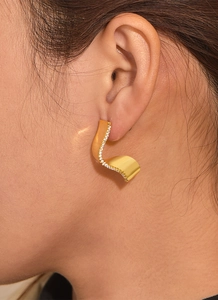 Detail shot of wavy gold-plated earrings with micro-set white zircon on a female ear