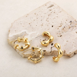 Detailed view of polished 18K gold-plated geometric sphere and wave design stud earrings