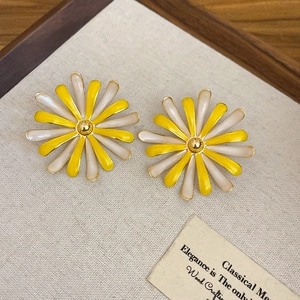 Dettaglio di orecchini a fiore in smalto giallo e crema su un vassoio di legno vintage