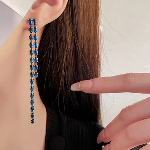 Detailed view of long gold tassel earrings with blue marquise-cut stones worn by a model