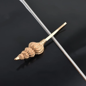 Detailed view of a golden conch shell hair clip with fine spiral metal texture and luster