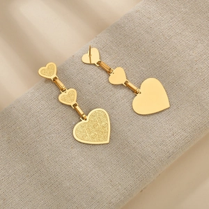 Vue détaillée montrant la texture mate des boucles d'oreilles pendantes triple cœur dorées