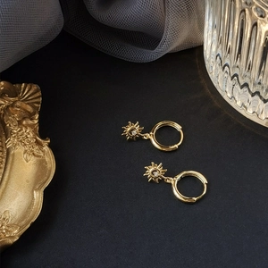 Detailed view of gold sunburst drop earring with shimmering zircon in a luxury setting