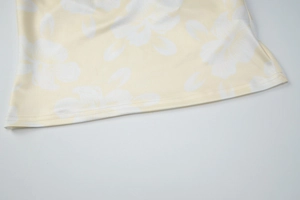 Close-up of yellow floral print fabric with white flower patterns and stitched hem detailing