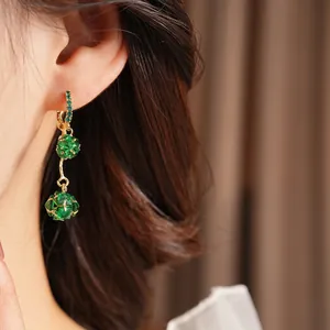 Vintage emerald green crystal ball drop earrings with gold hooks on a model