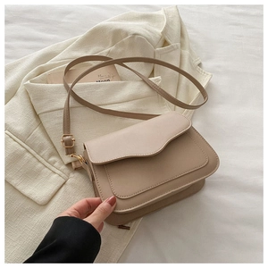Detail showing beige crossbody bag with adjustable strap and golden buckle on white fabric