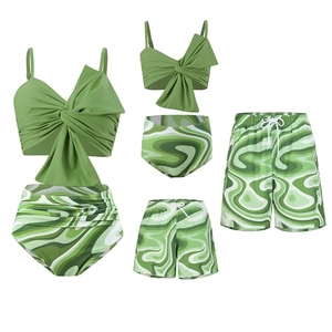 Flat lay of family matching swimwear with green abstract wave prints on white backdrop