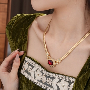 Close-up of vintage gold snake chain necklace with large red oval gemstone on a model
