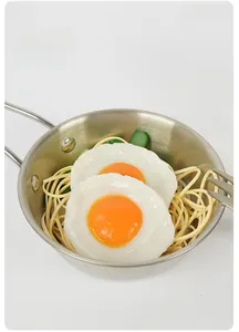 Vista dettagliata di uova al tegamino artificiali e pasta in una mini padella in acciaio