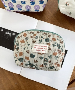 Quilted floral cosmetic bag with green zipper detail shown on a desk background